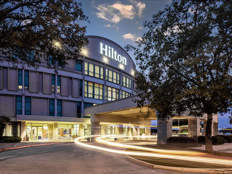 A modern hotel with a prominent 'Hilton' sign, a covered entrance, and a well-lit facade.