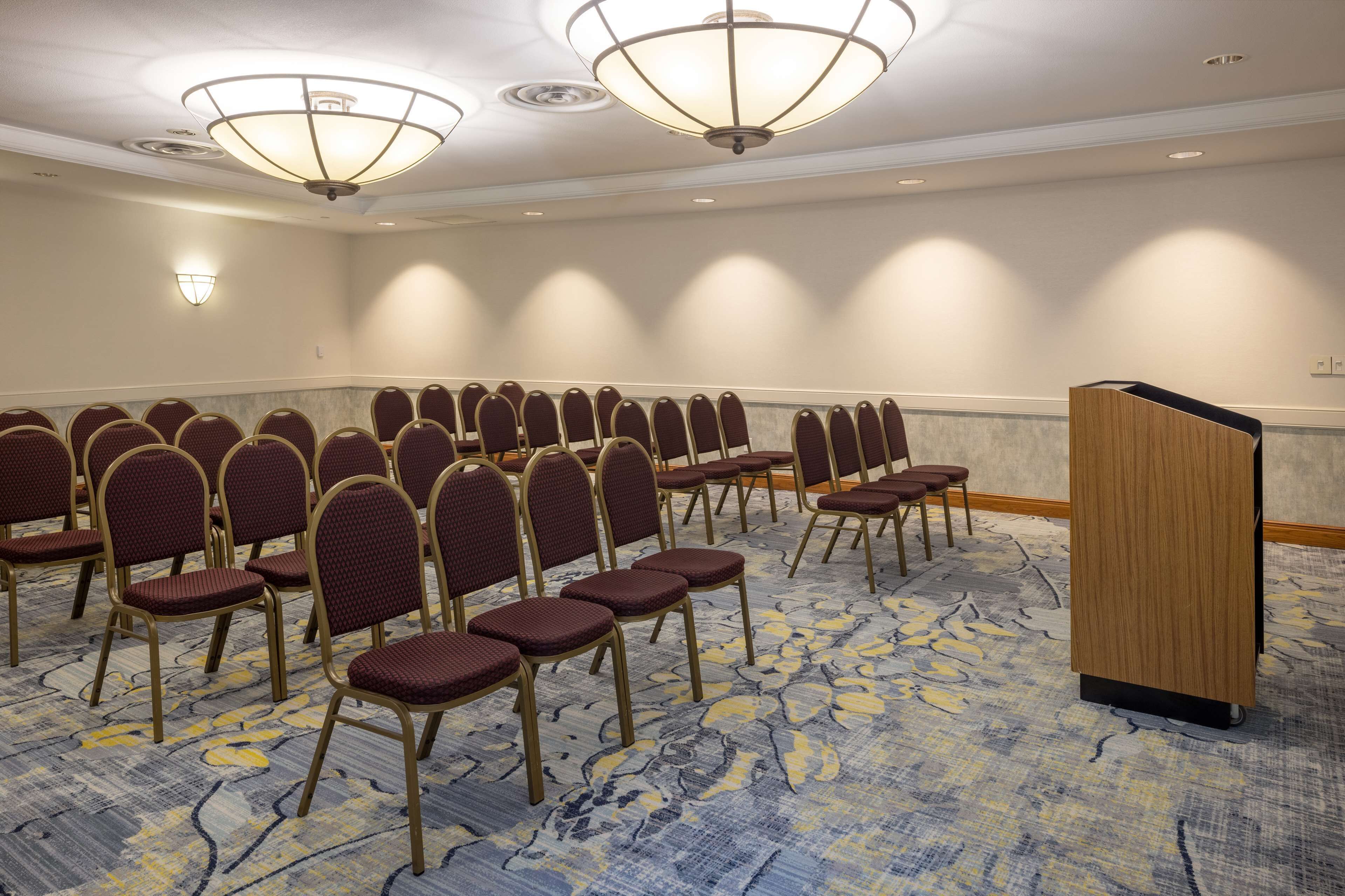 A conference room with rows of chairs, a podium, and ceiling lights.