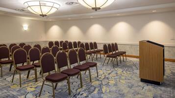 A conference room with rows of chairs, a podium, and ceiling lights.