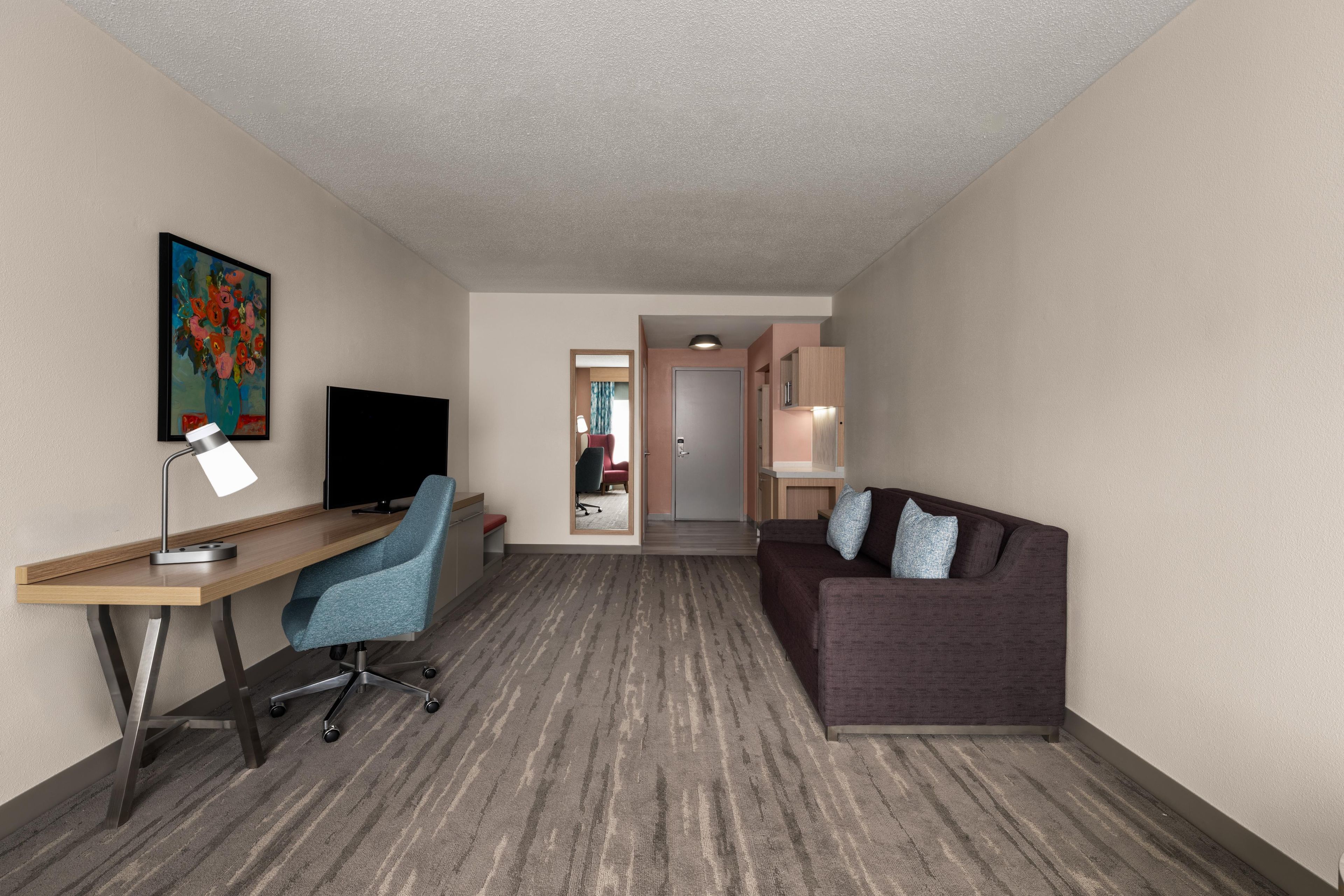 A hotel room with a desk, chair, television, and a sofa.