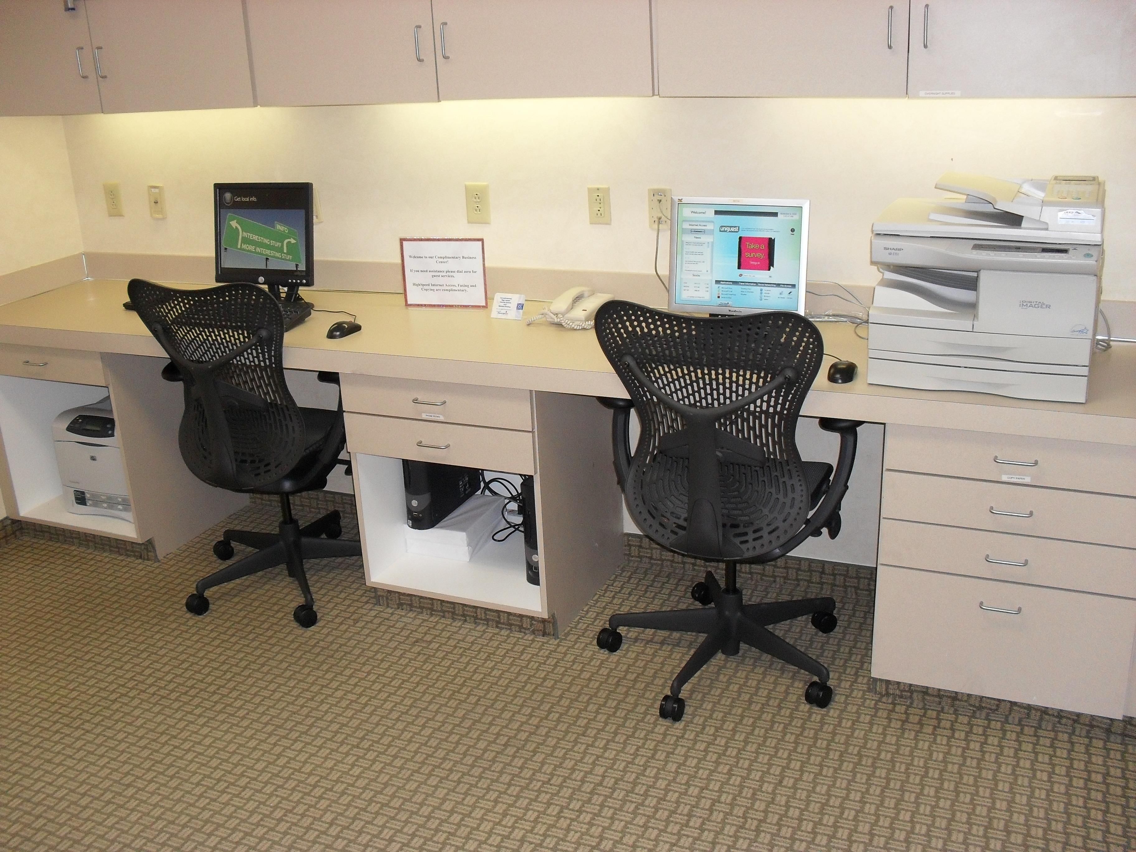 A workspace with two office chairs, a desk, a computer monitor, a printer, and a sign on the wall.
