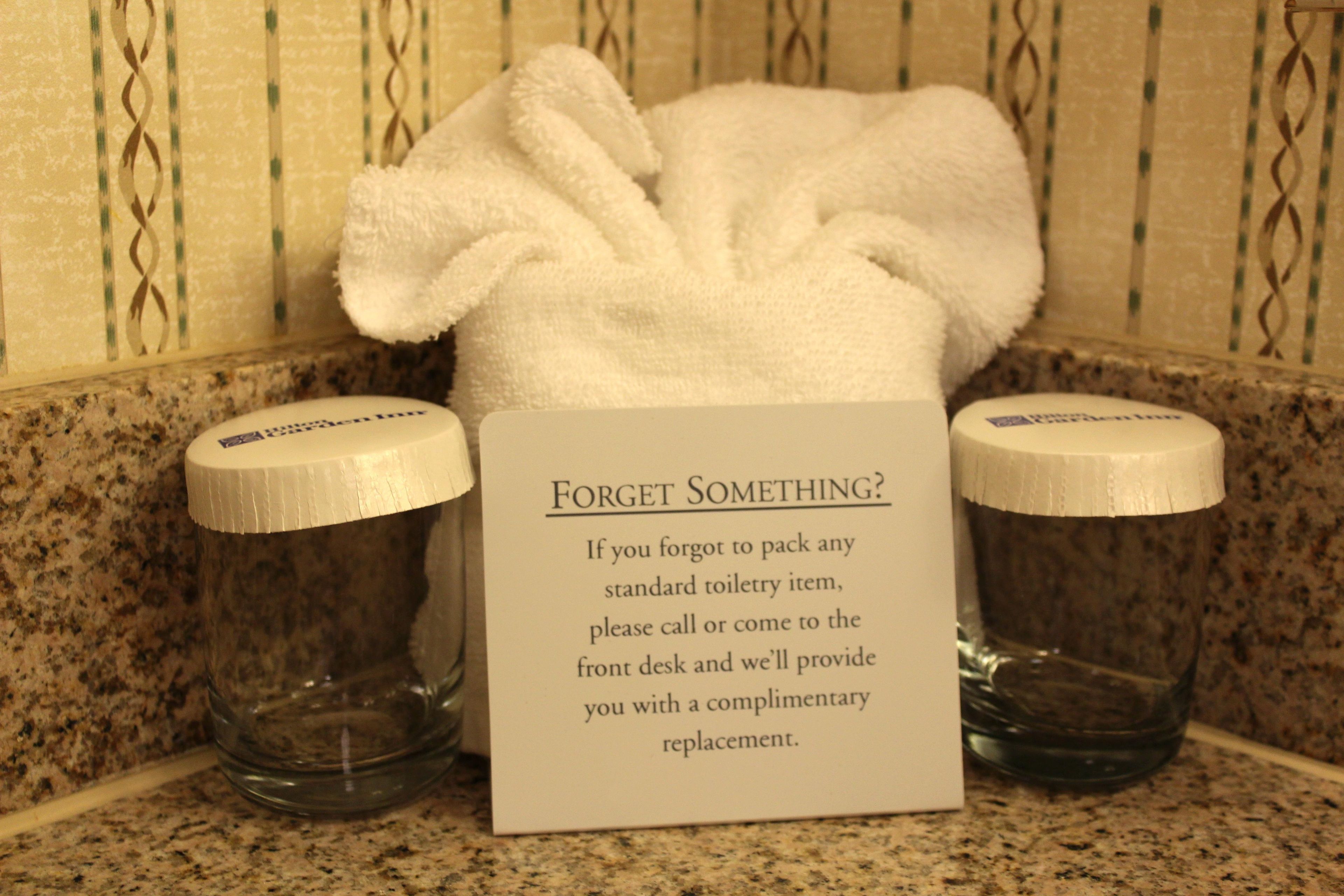 A bathroom with a sign offering complimentary toiletries if guests forget to pack any standard toiletry item.
