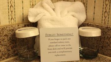 A bathroom with a sign offering complimentary toiletries if guests forget to pack any standard toiletry item.