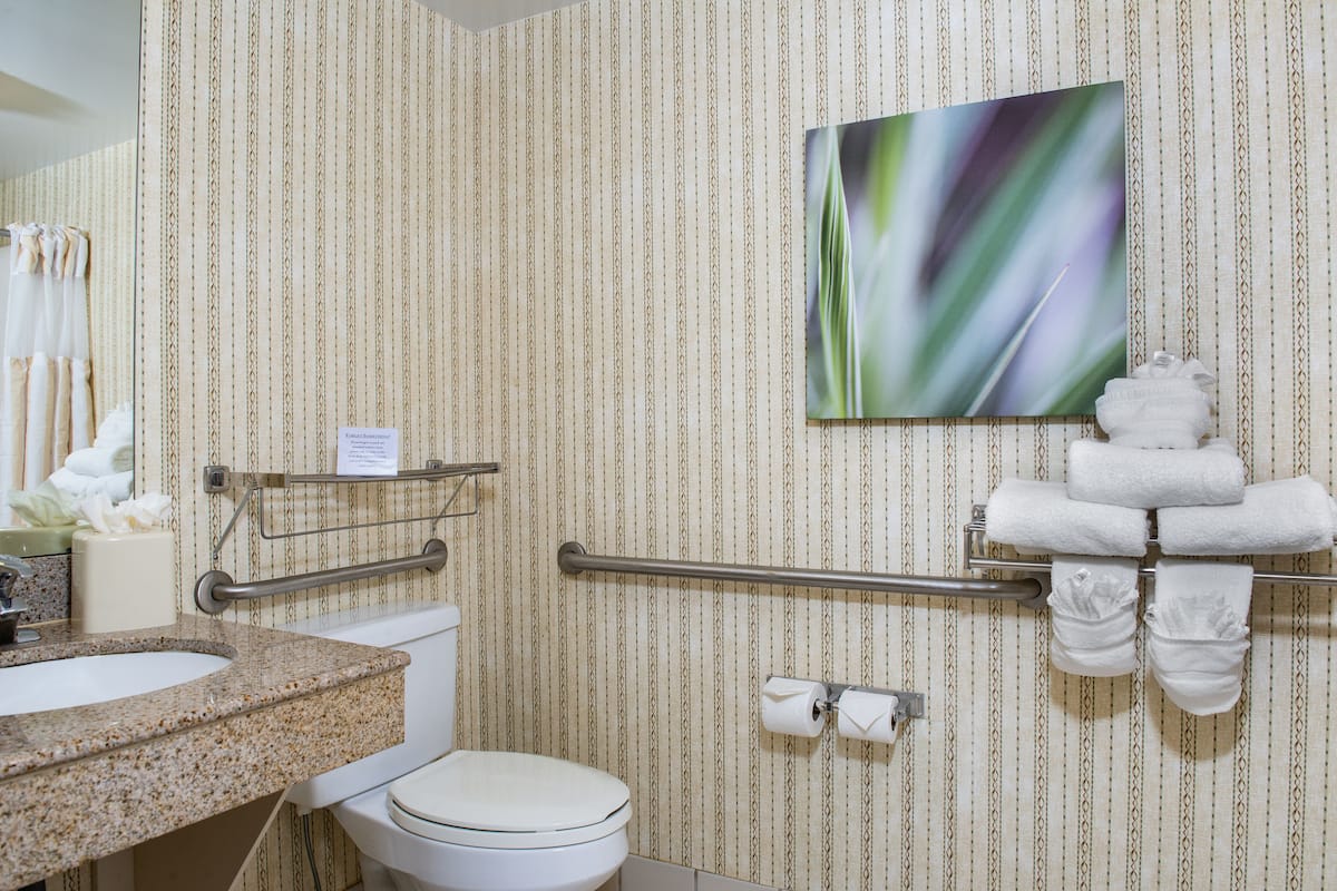 A bathroom with a striped wallpaper, a sink with a granite countertop, a toilet, a towel rack with towels, and a painting on the wall.
