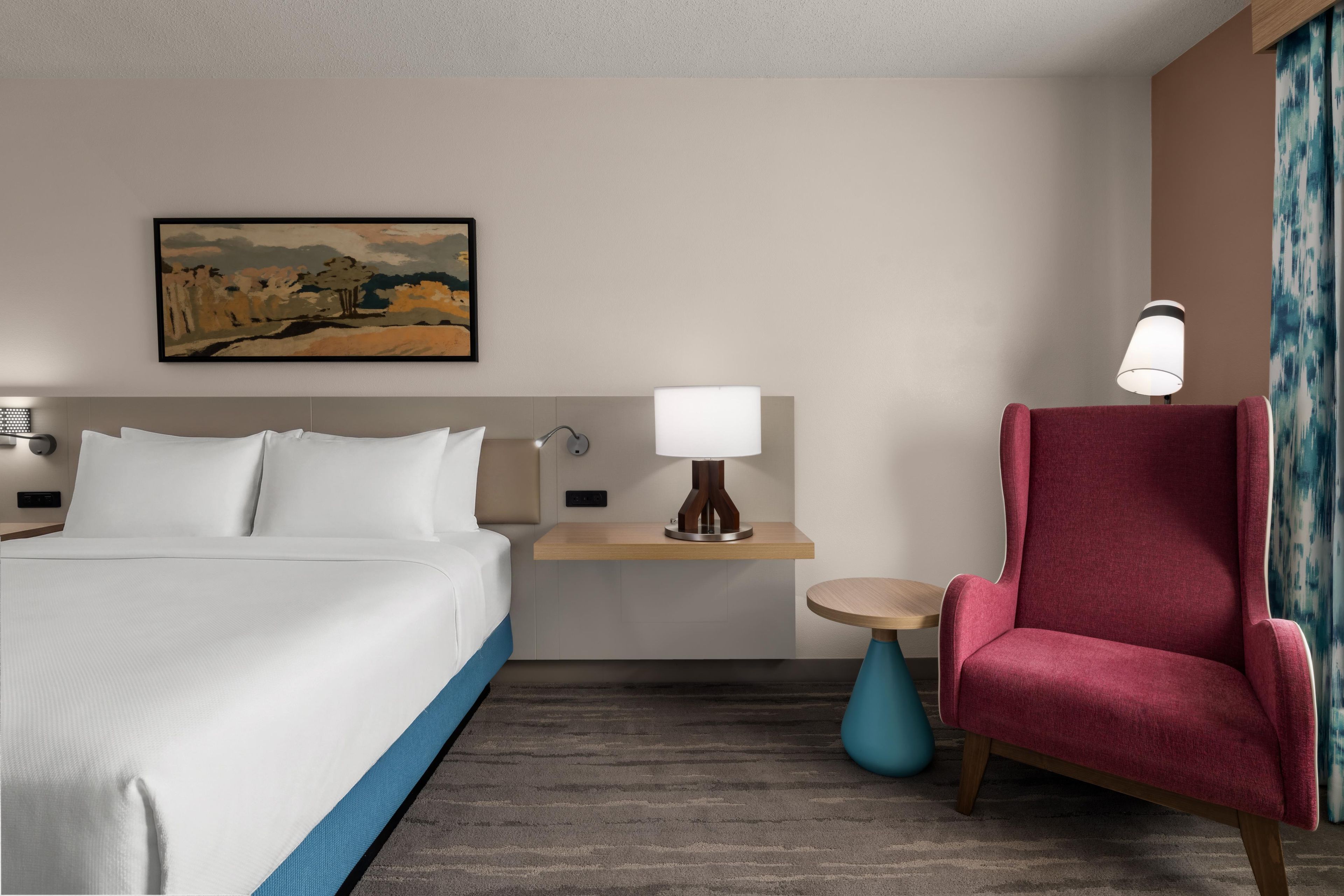 A hotel room with a bed, a desk, a chair, and a painting on the wall.