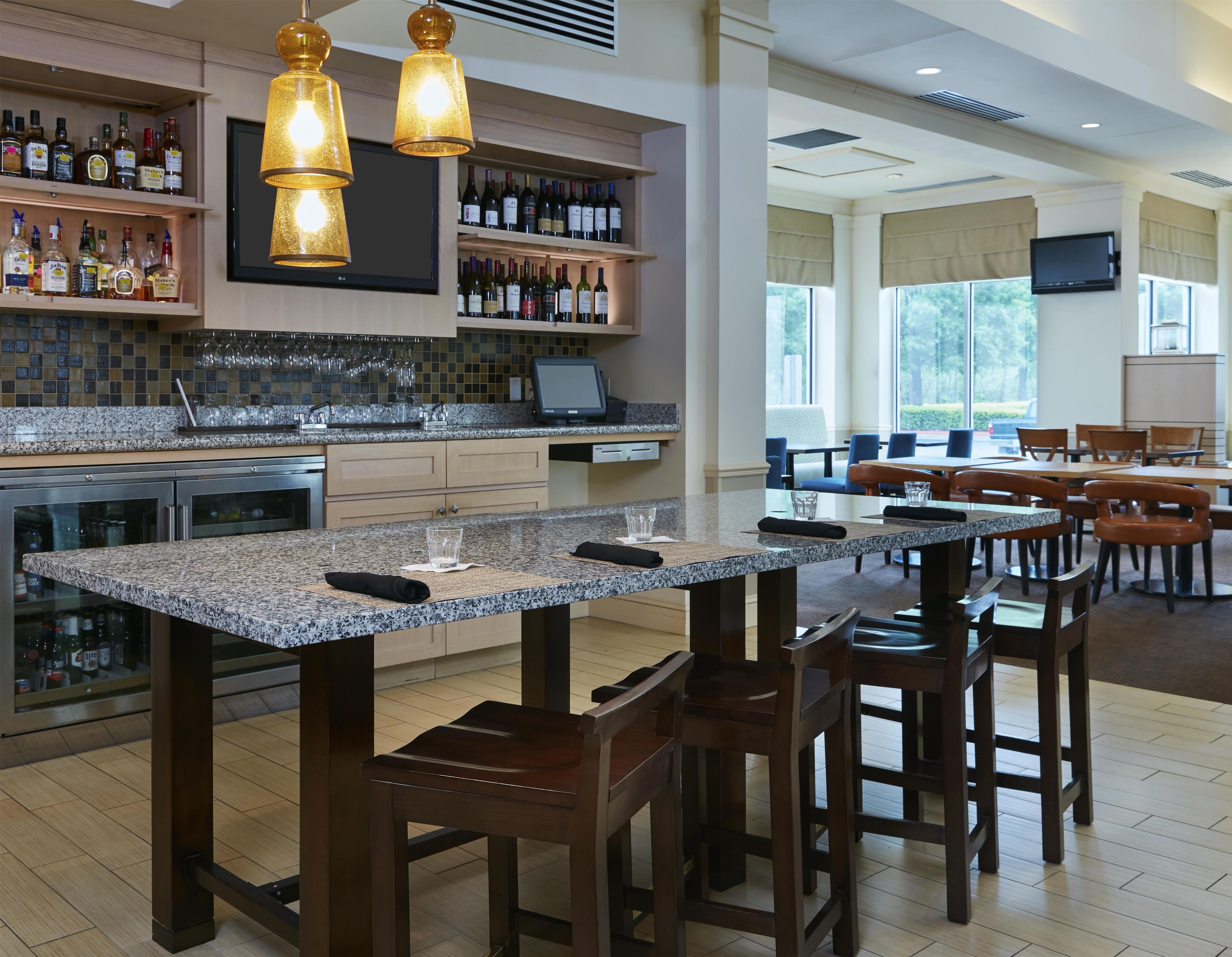 A hotel bar with a granite countertop, wooden chairs, and a wine bottle display.