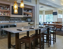 A hotel bar with a granite countertop, wooden chairs, and a wine bottle display.