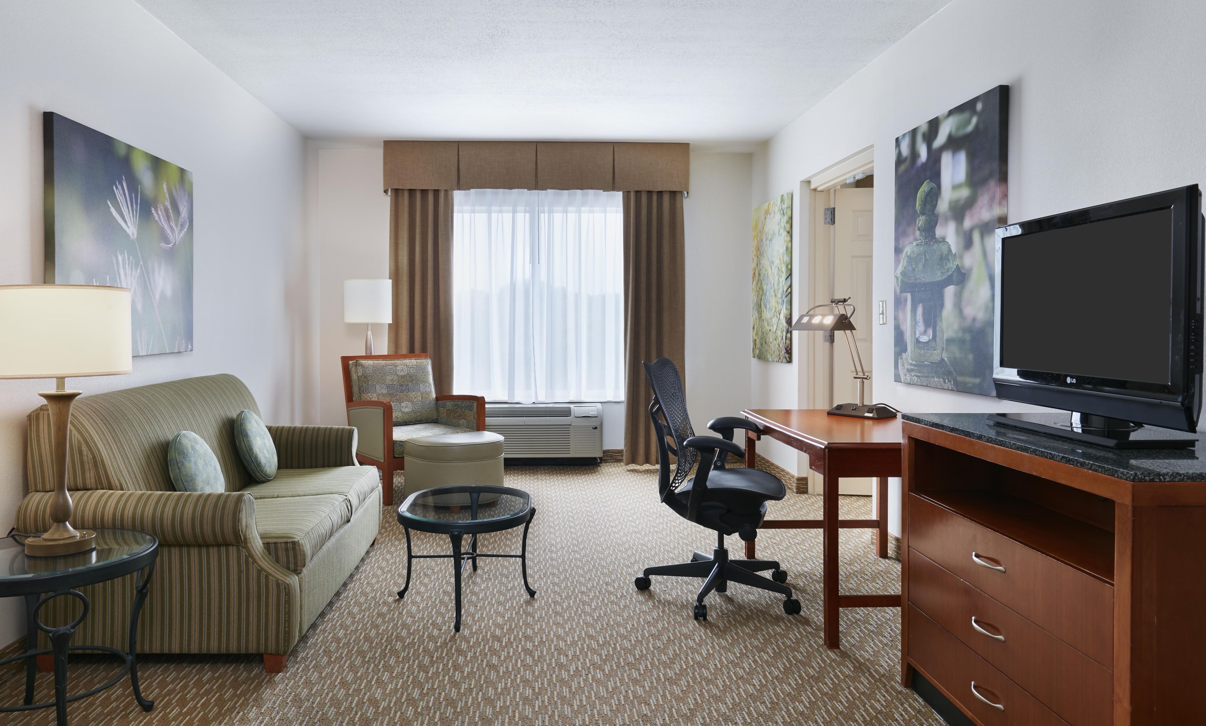 A hotel room with a sofa, a desk with a computer, a television, and artwork on the walls.