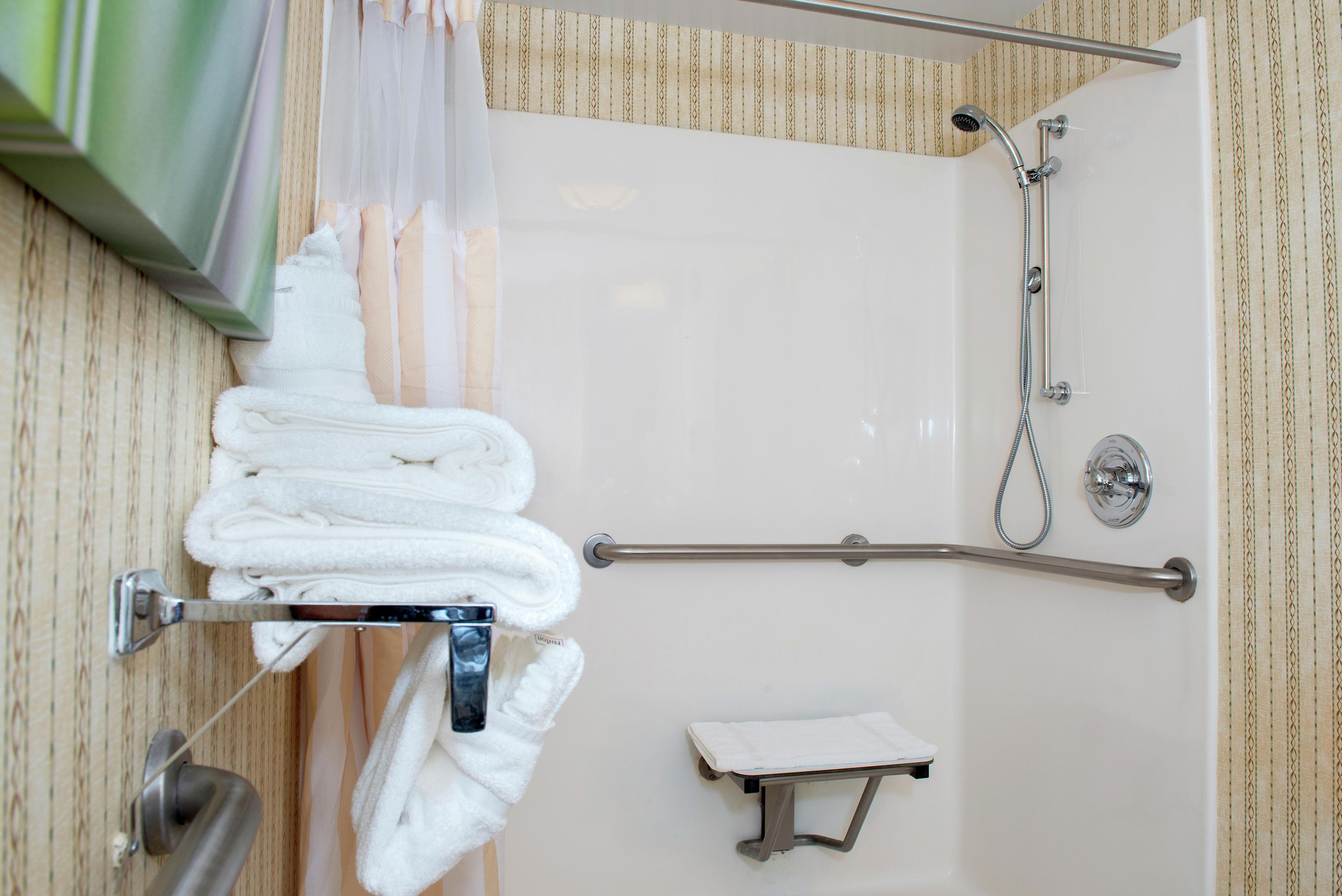 A bathroom with a shower, a towel rack with folded towels, and a small stool.
