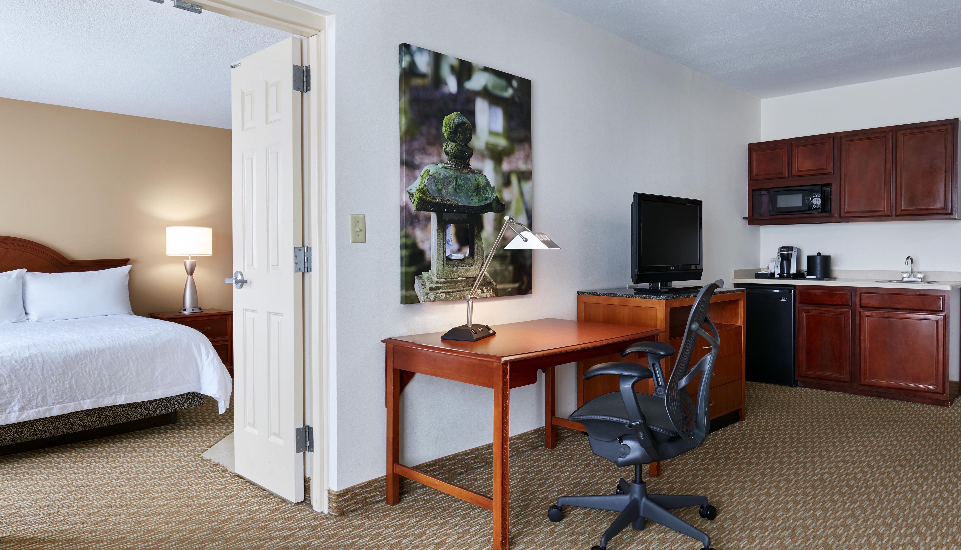 Une chambre d’hôtel équipée d’un lit, d’un bureau, d’une chaise, d’une télévision et d’une kitchenette.