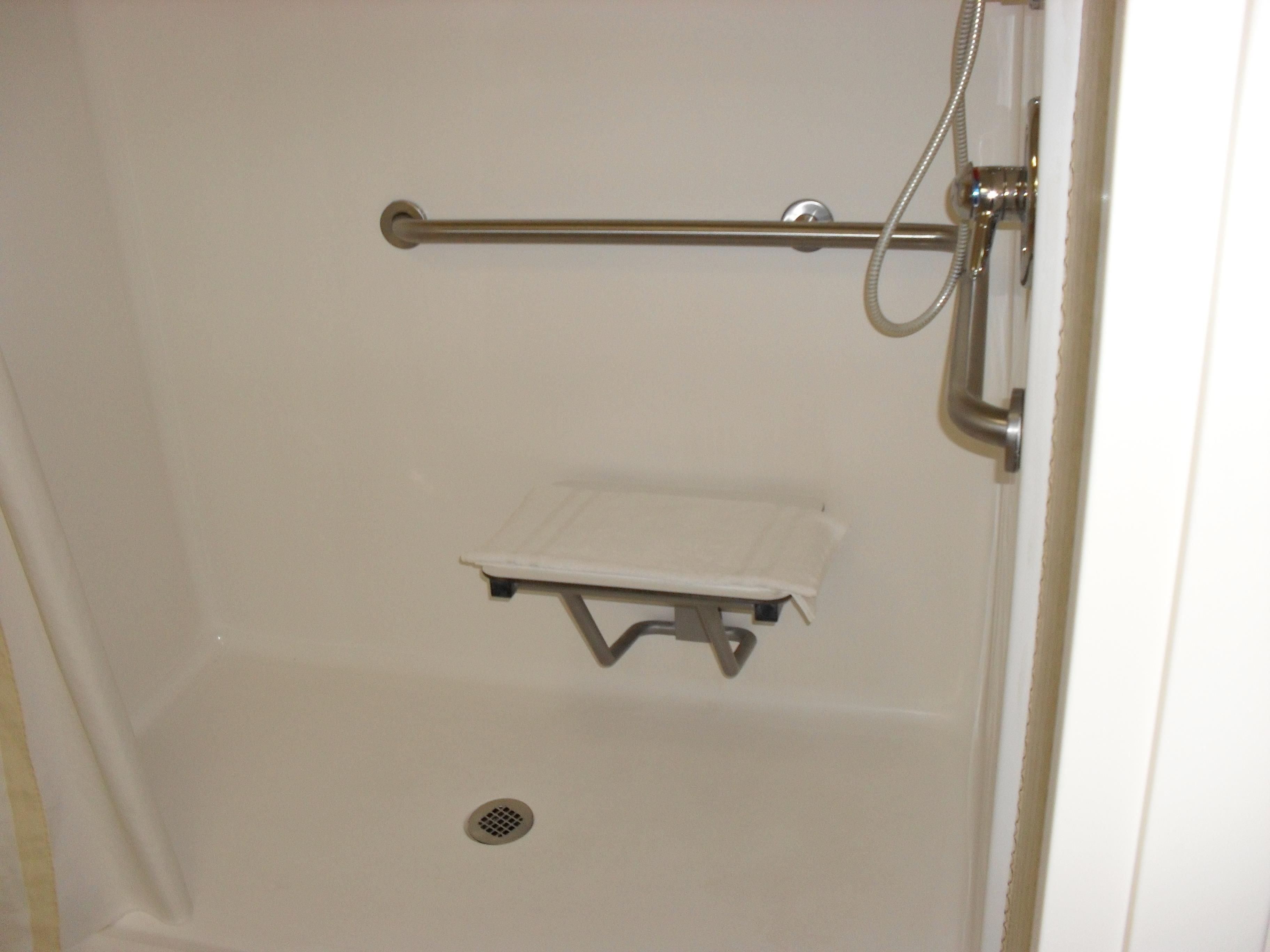 A shower stall with a grab bar, a small shelf, and a drain.