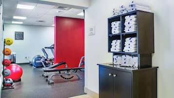 Un gimnasio con equipo de ejercicio, una pared roja y un estante con toallas.