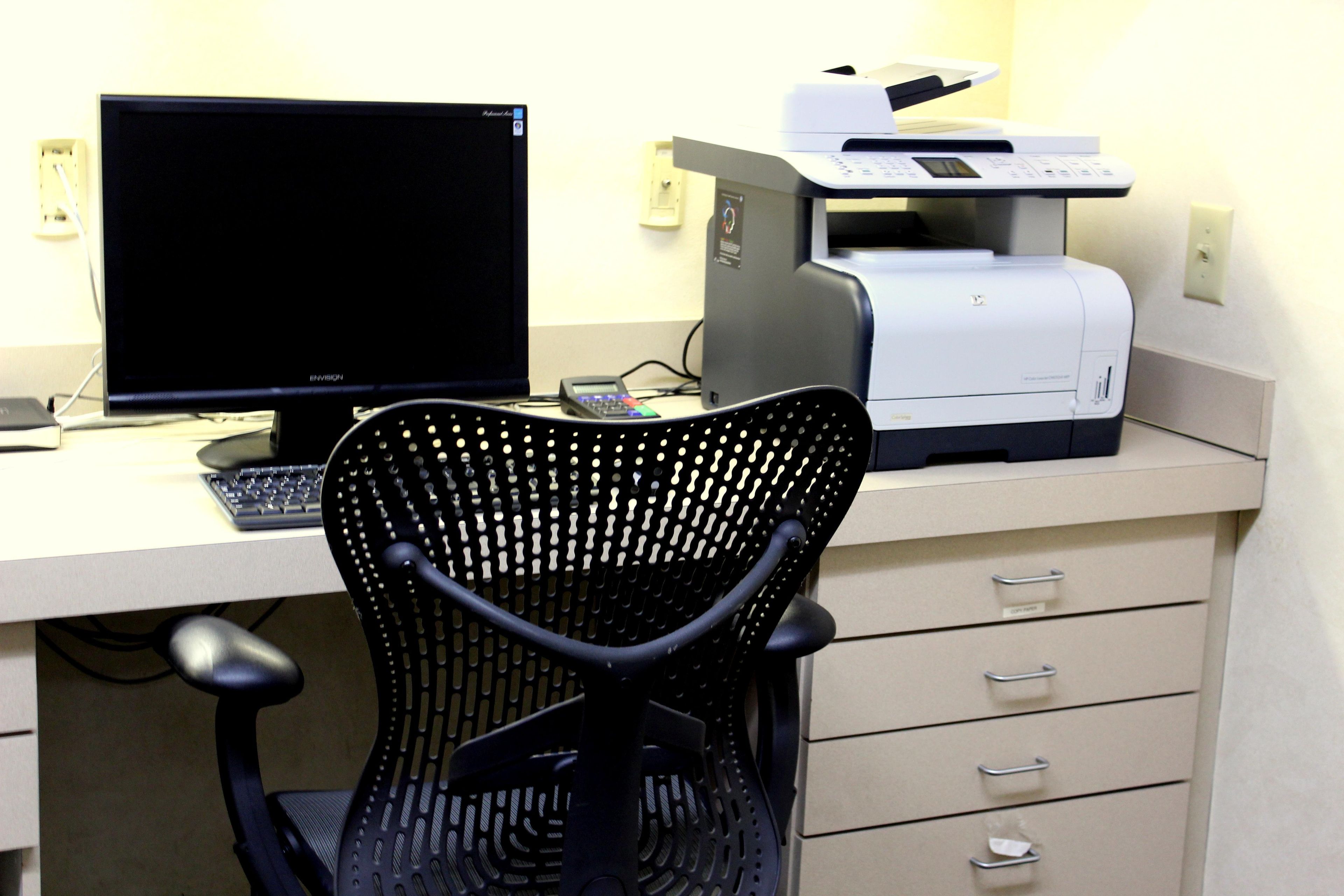 A computer desk with a monitor, keyboard, and printer.