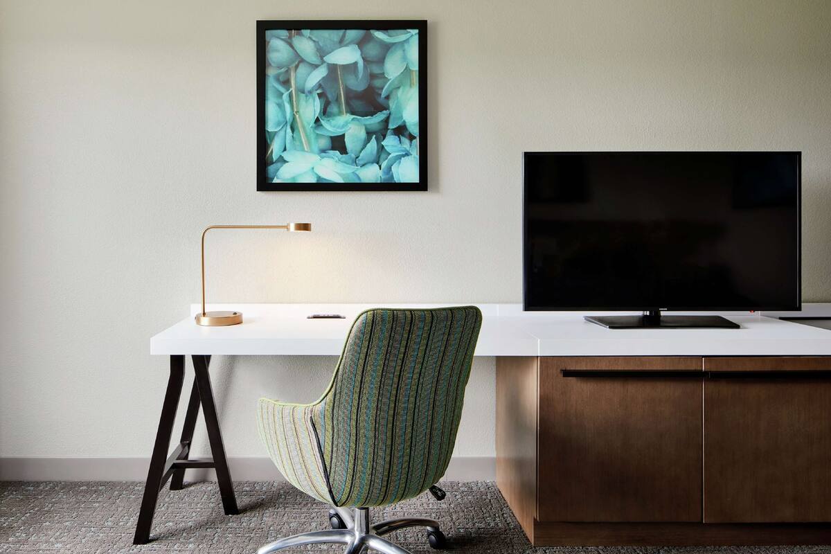 A modern office desk with a computer monitor, a green-striped office chair, and a floor lamp.