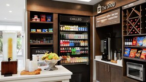 A kitchenette area with a coffee machine, a refrigerator labeled 'CHILLED' and 'FROZEN', and shelves stocked with snacks and condiments. - Hilton Garden Inn Cincinnati Northeast (Loveland)