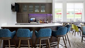 A bar area with a counter, bar stools, and a television. There are cabinets above the counter and a view of the outside through large windows. - Hilton Garden Inn Cincinnati Northeast (Loveland)