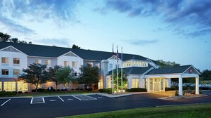 A hotel with a covered entrance, flagpoles, and a parking lot. - Hilton Garden Inn Cincinnati Northeast (Loveland)
