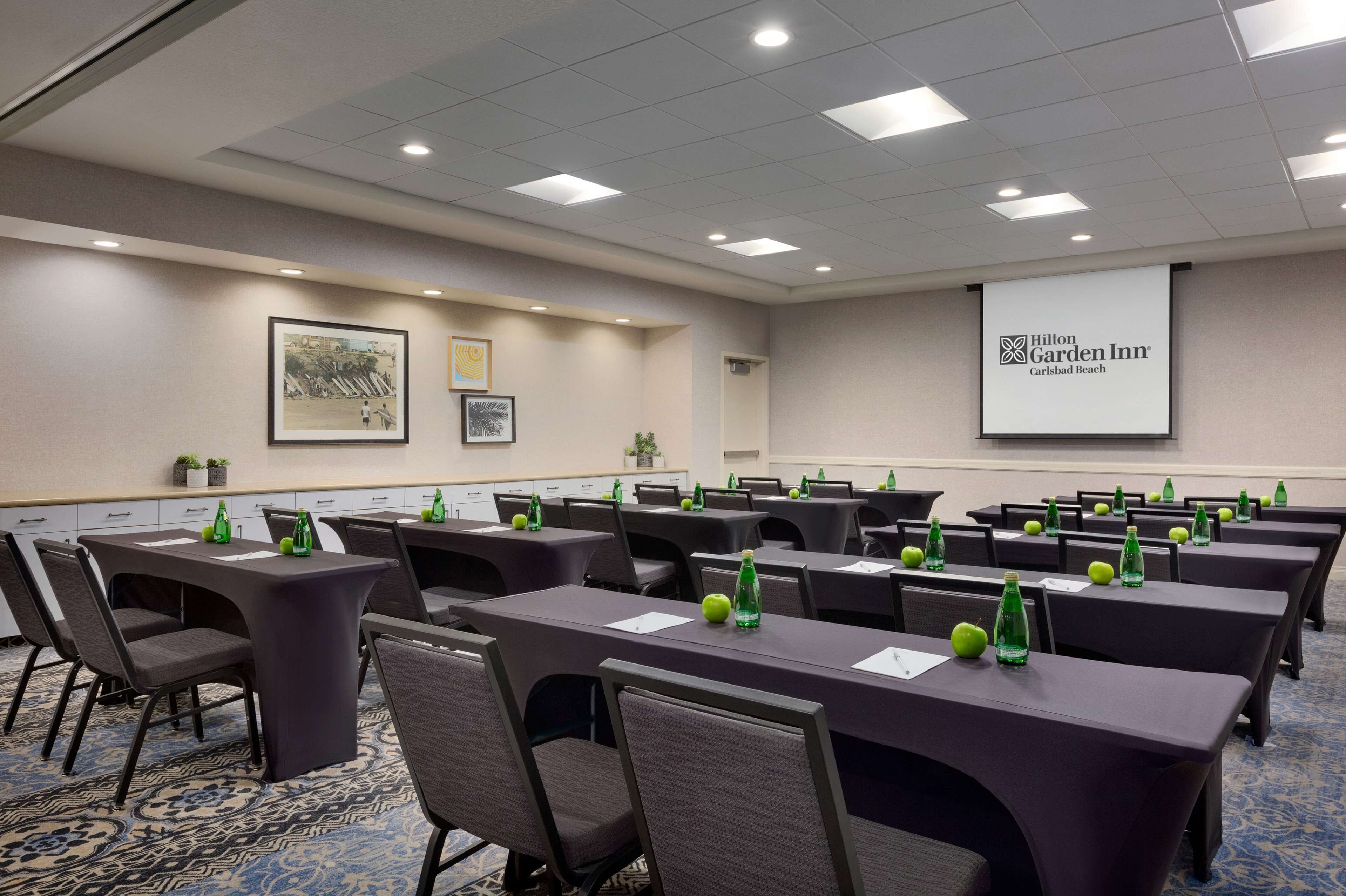 A conference room with tables, chairs, and a projector screen displaying the Hilton Garden Inn logo.