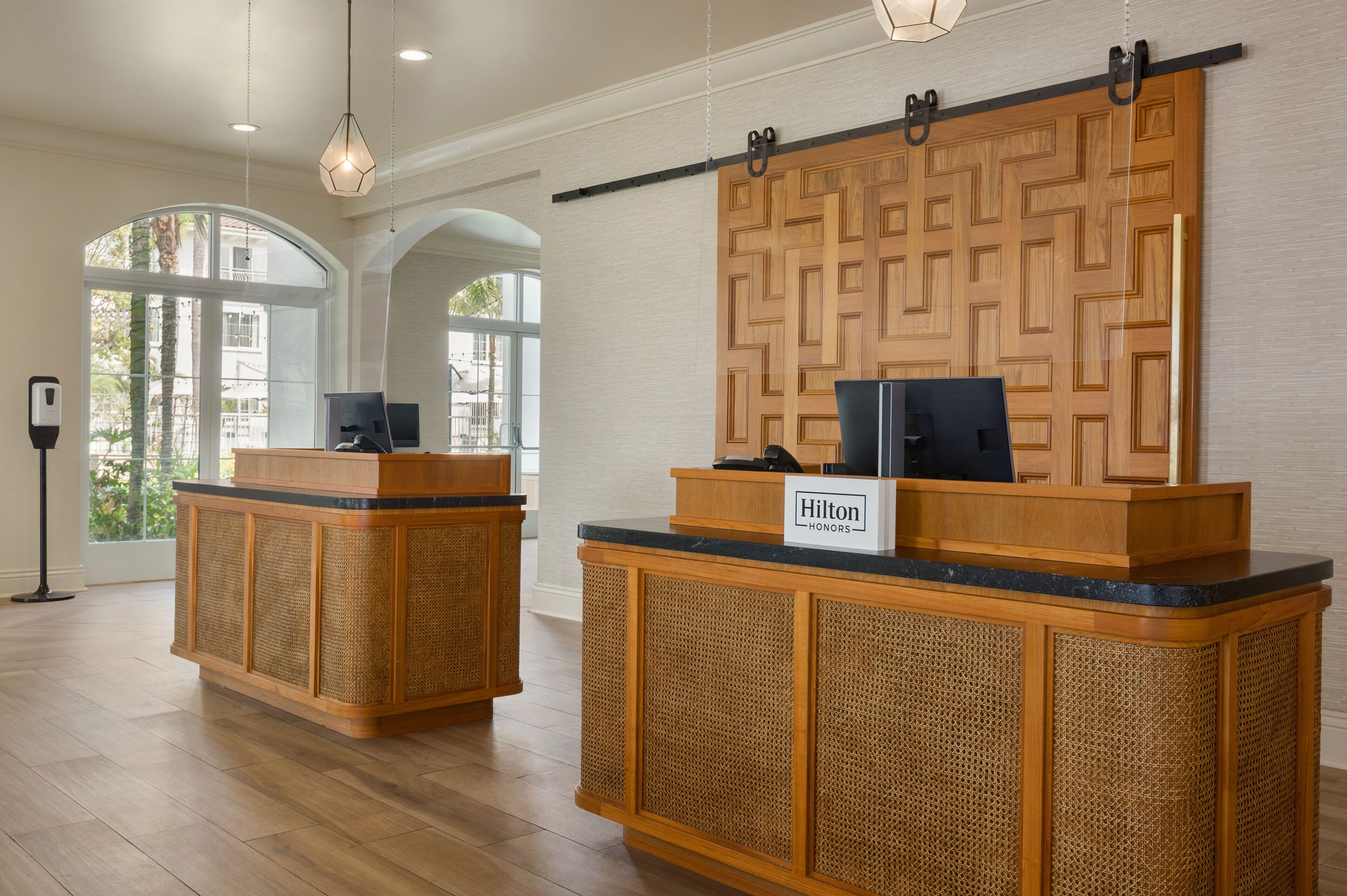 Un espace d’accueil comprenant deux comptoirs de réception en bois, un téléviseur fixé au mur et un panneau indiquant « Hilton Honors ».