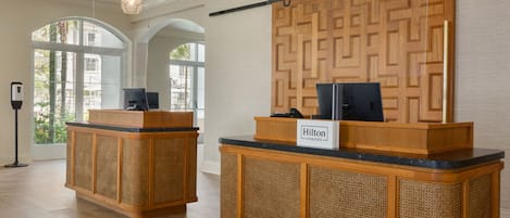 Un área de recepción con dos mostradores de madera, un televisor montado en la pared y un letrero que dice "Hilton Honors".