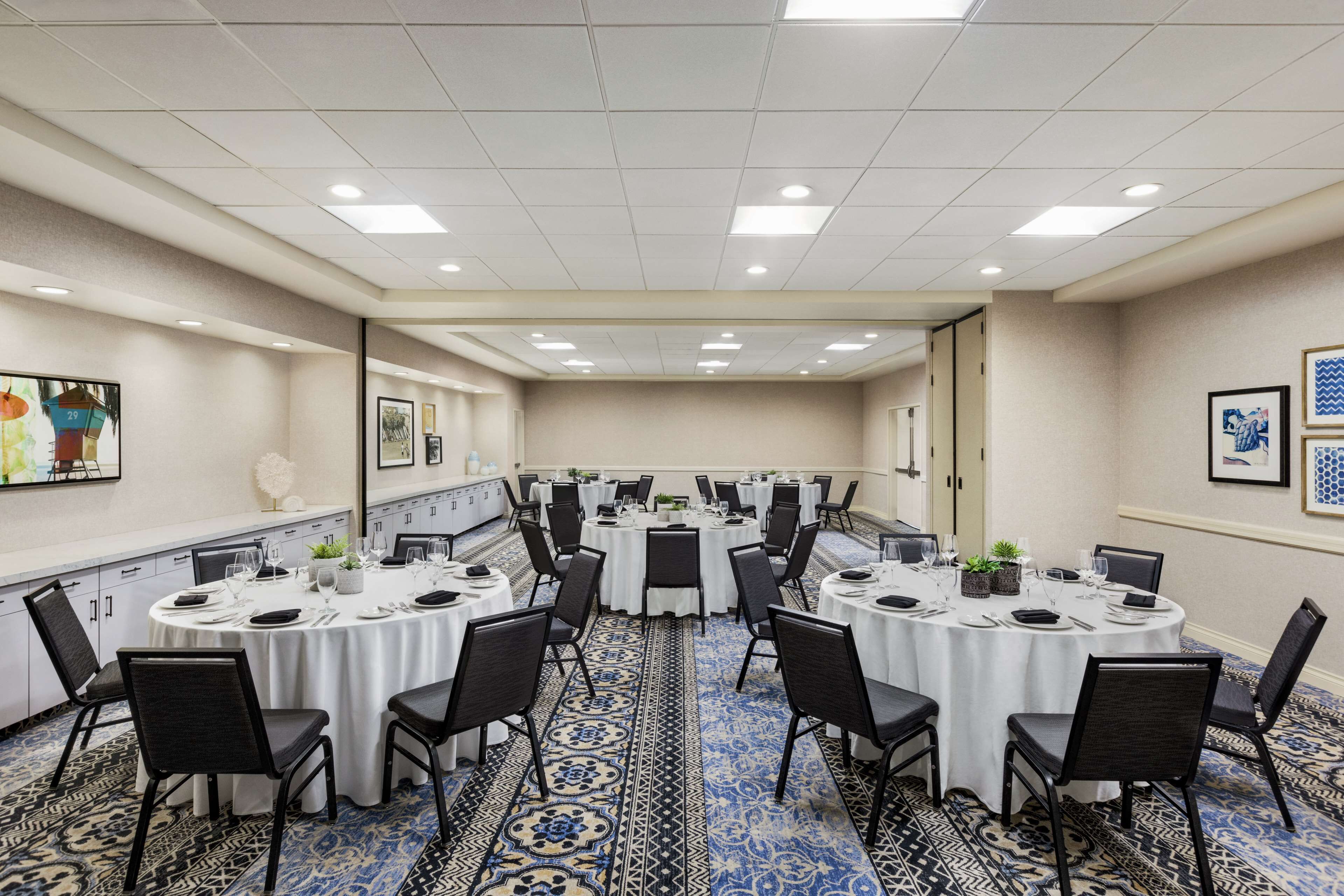 A conference room with multiple round tables, black chairs, and a patterned carpet.