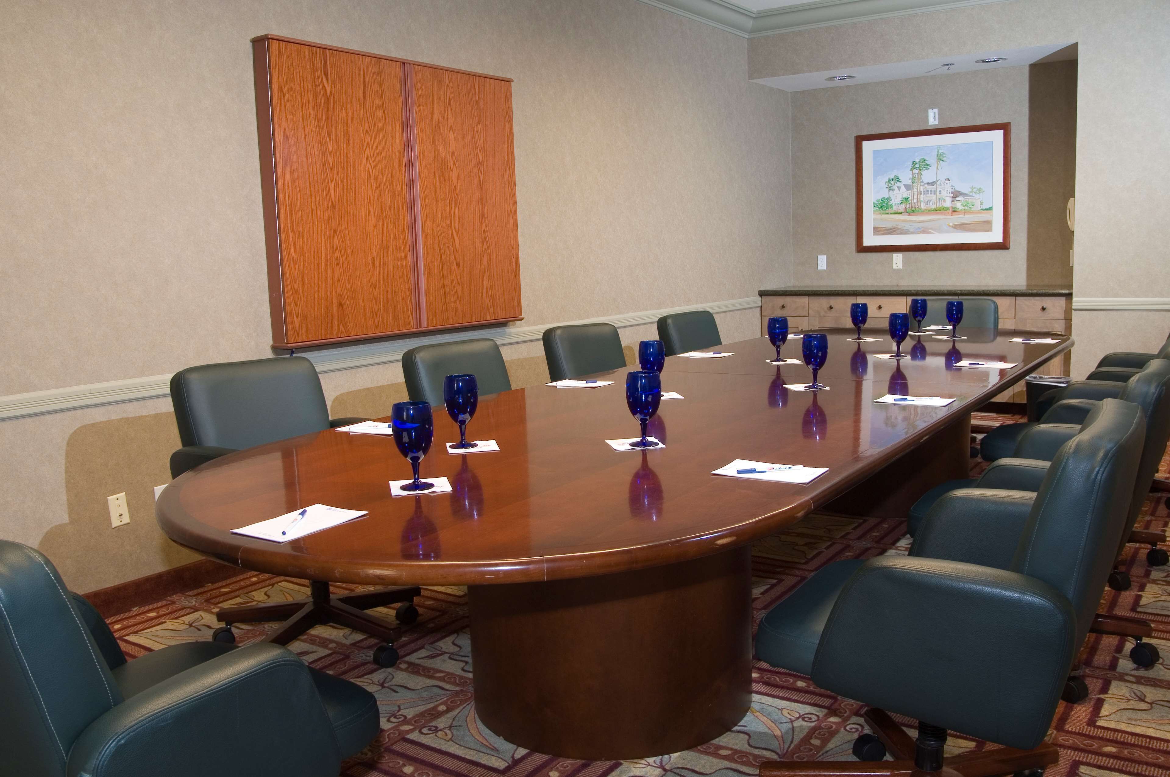 A conference room with a large oval table, multiple chairs, and blue wine glasses.