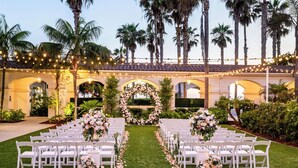 An outdoor wedding venue with rows of white chairs, a floral archway, and string lights.