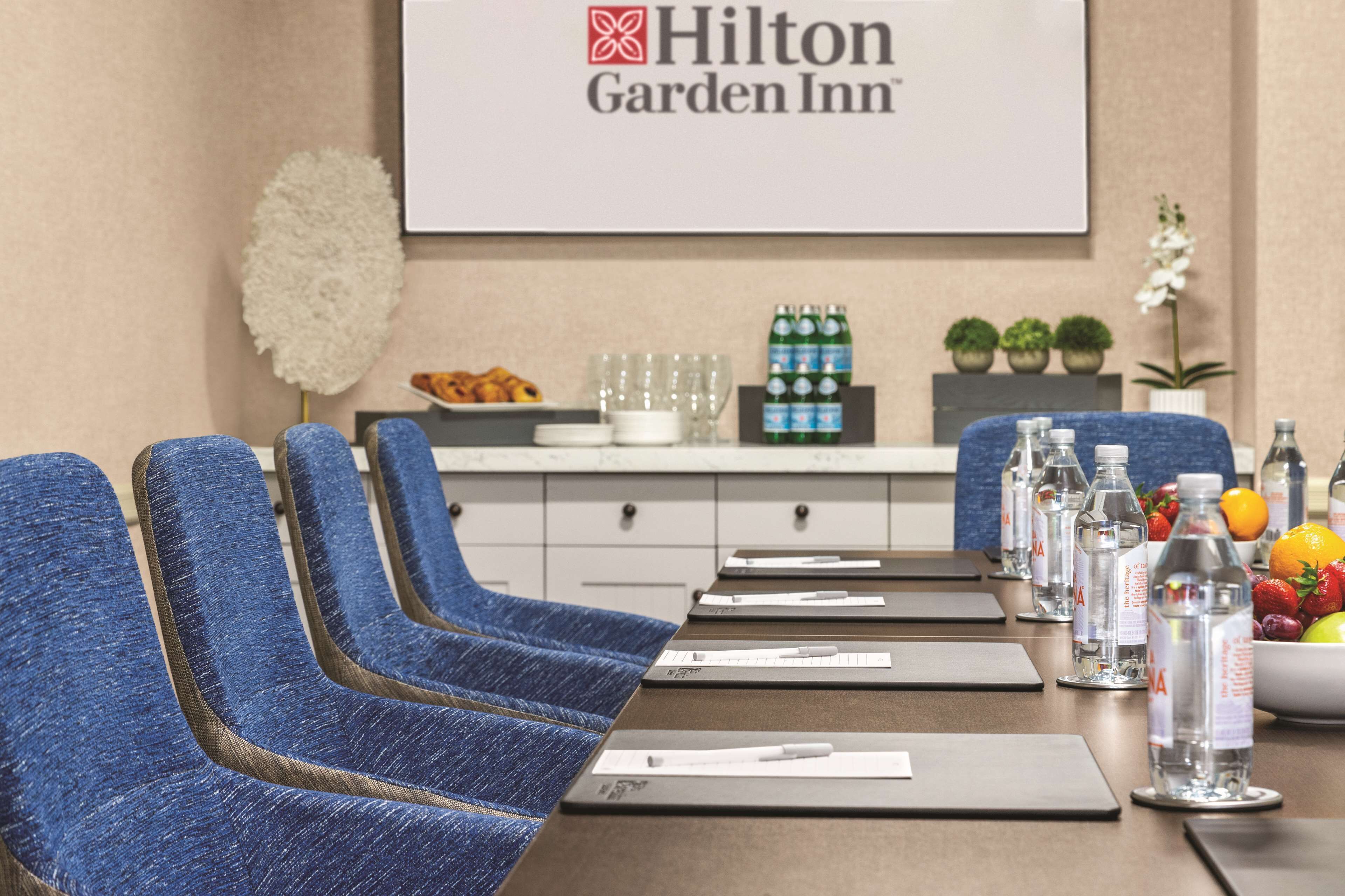 Une salle de conférence avec des chaises bleues, une table sur laquelle sont disposés des cartes de nom, des bouteilles d’eau et un saladier de fruits.