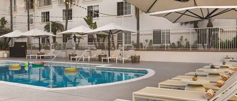 A poolside area with lounge chairs, umbrellas, and a swimming pool.