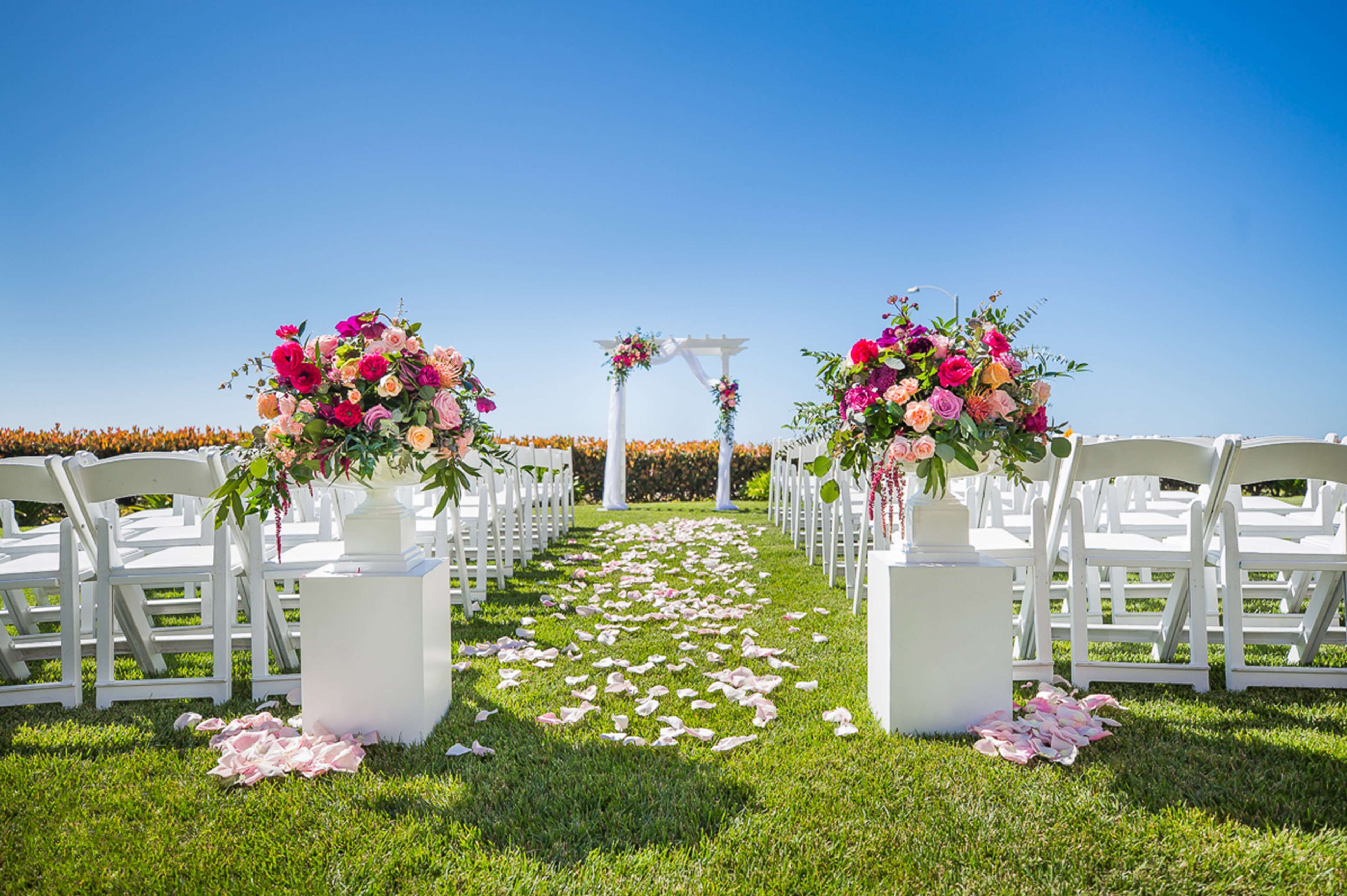 Une allée de cérémonie de mariage agrémentée de chaises blanches et de compositions florales.