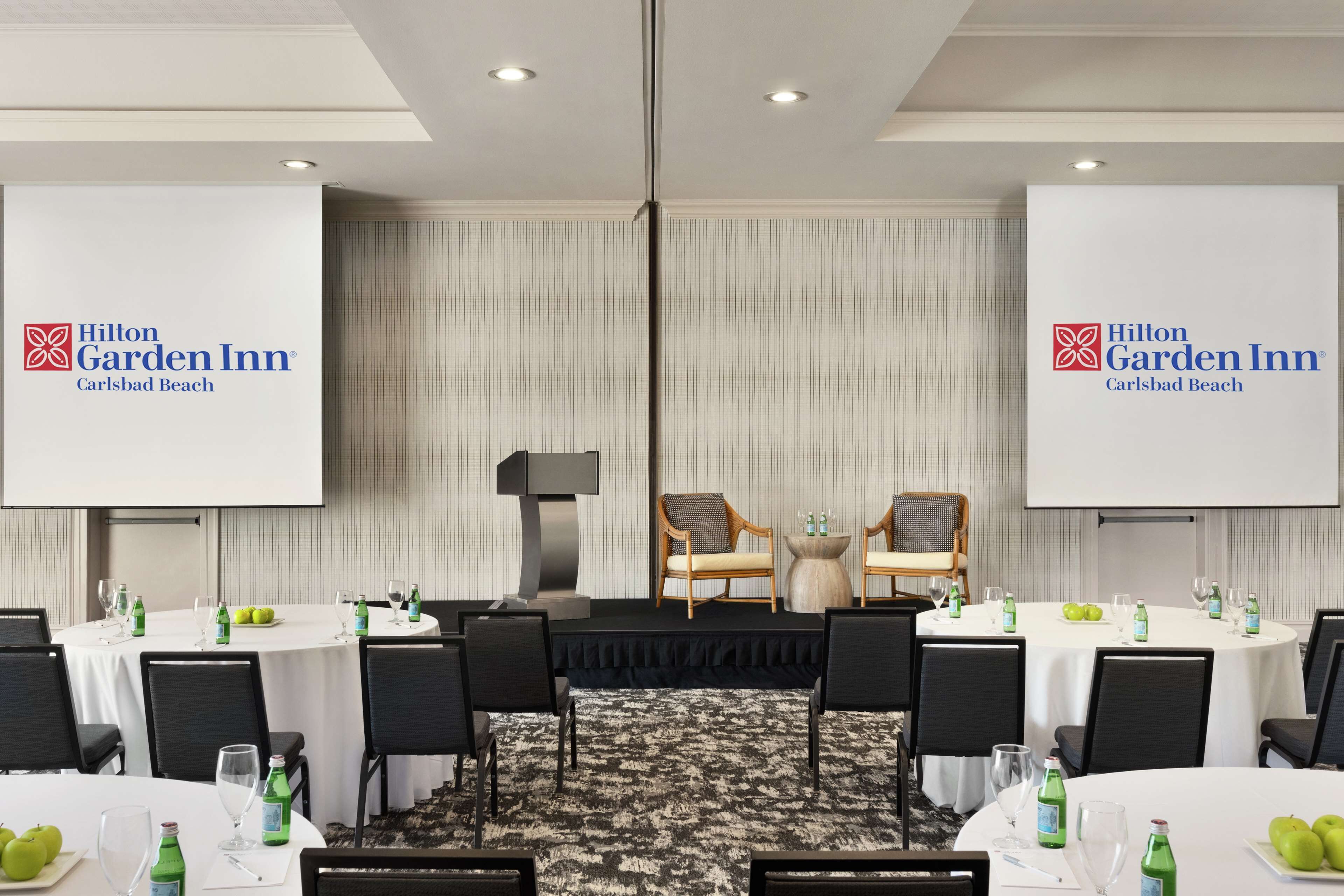 Uma sala de conferências no Hilton Garden Inn, com várias mesas, cadeiras e telas de apresentação.