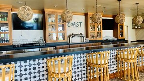 A bar area with a long counter, wicker chairs, and decorative hanging lights.