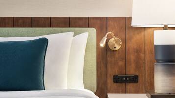 A neatly made bed with white and teal pillows, a green headboard, a wall-mounted lamp, and a power outlet on a wooden panel wall.