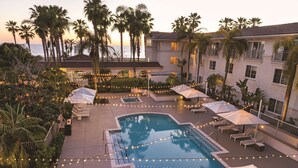 A pool area with lounge chairs and umbrellas, surrounded by palm trees and a building with balconies.