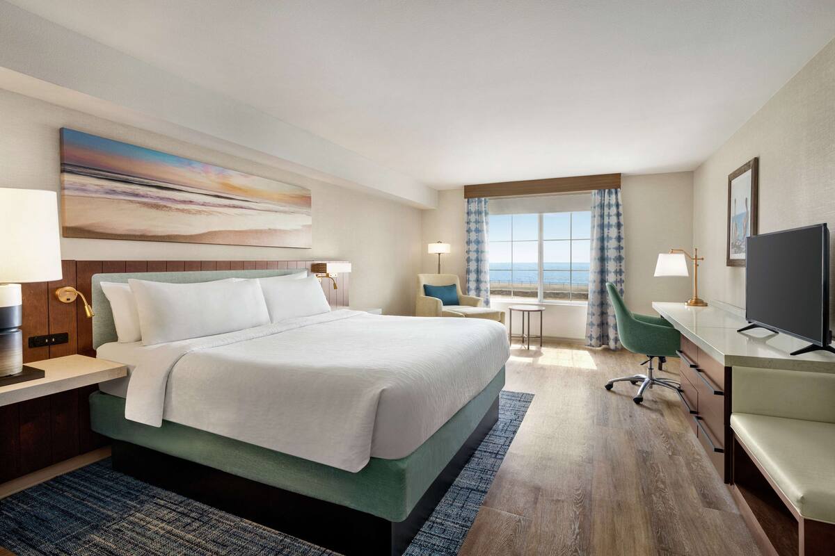 A hotel room with a bed, a desk, a chair, a TV, and a window with curtains.