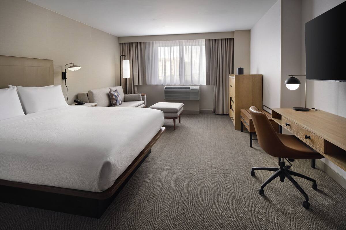 Une chambre d’hôtel avec un grand lit, un bureau, une chaise, une armoire et un téléviseur.