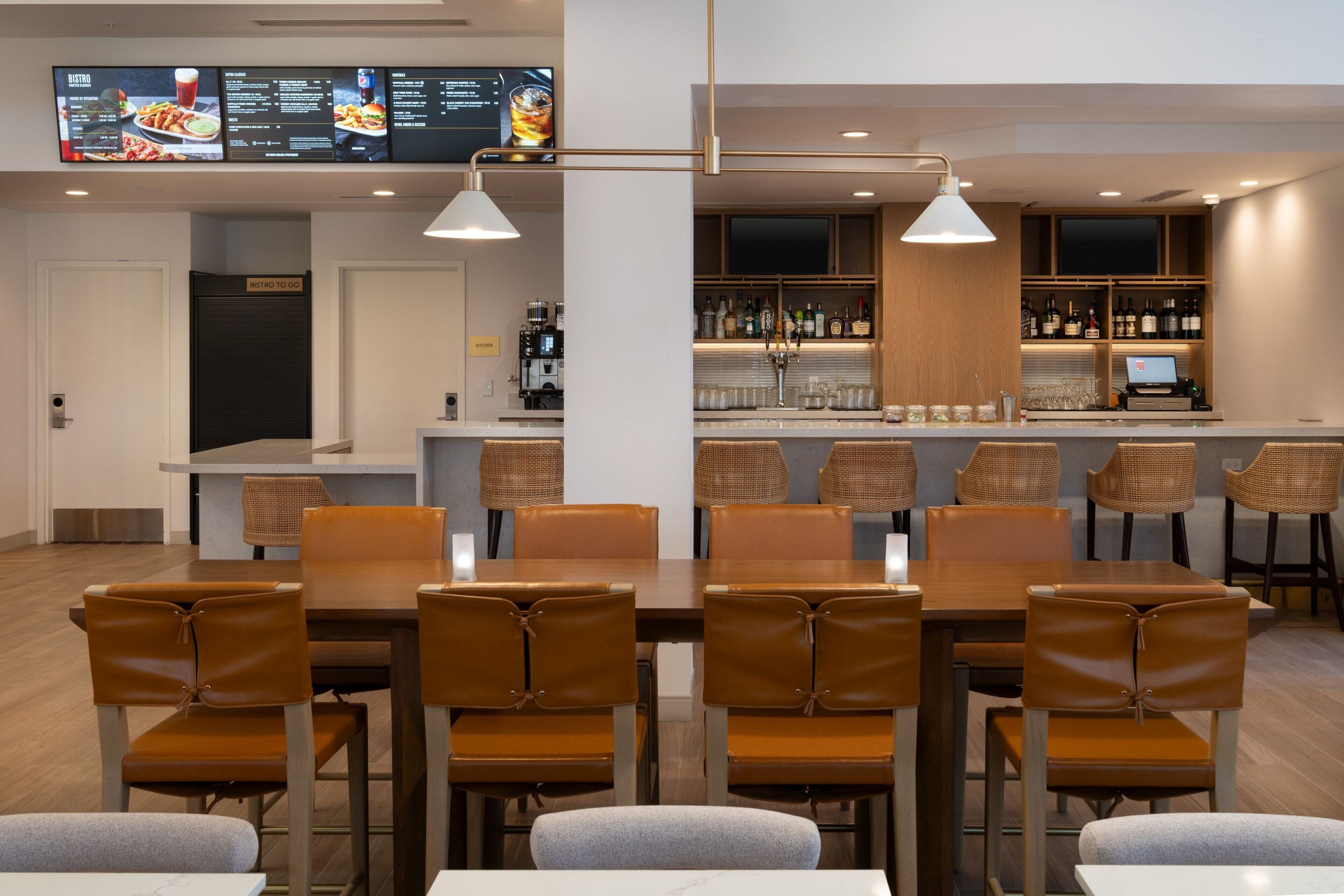 Un restaurante moderno con una zona de bar, mesas y sillas de madera.