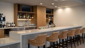 Un espace bar moderne, doté d’un long comptoir, de tabourets de bar en osier et d’étagères remplies de bouteilles et de verres.