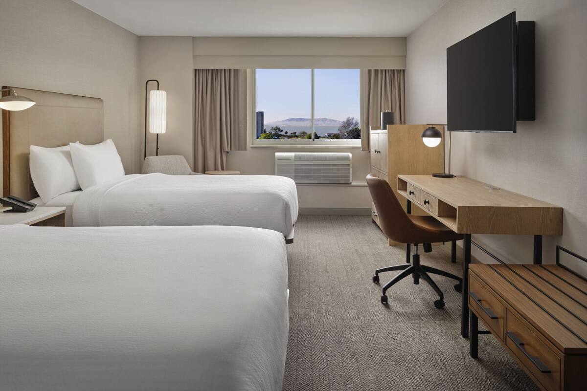 Une chambre d’hôtel avec deux lits, un bureau, une chaise, une télévision et une fenêtre donnant sur une vue sur la montagne.