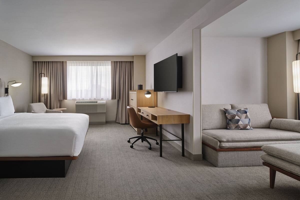 Une chambre d’hôtel avec un lit, un bureau, un canapé et une télévision.
