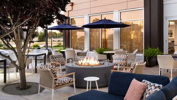 Un espace extérieur aménagé avec un foyer, des fauteuils en osier et des parasols.