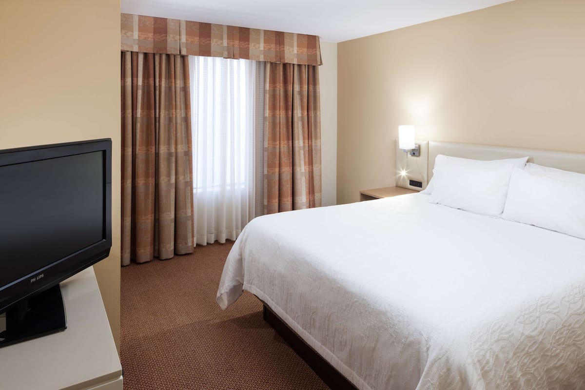 A hotel room with a bed, a TV, a nightstand, and curtains.