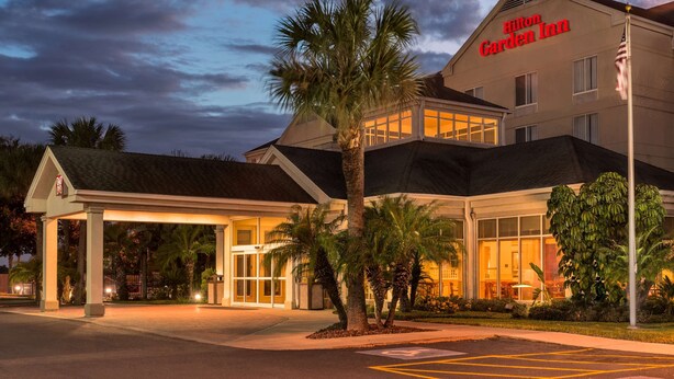 Un hotel con entrada cubierta, palmeras y un cartel que dice 'Hilton Garden Inn'.