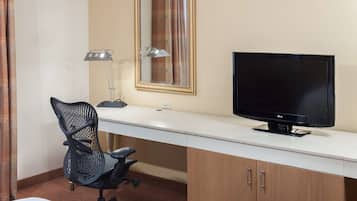 A hotel room with a desk, a chair, a television, a lamp, and a mirror.