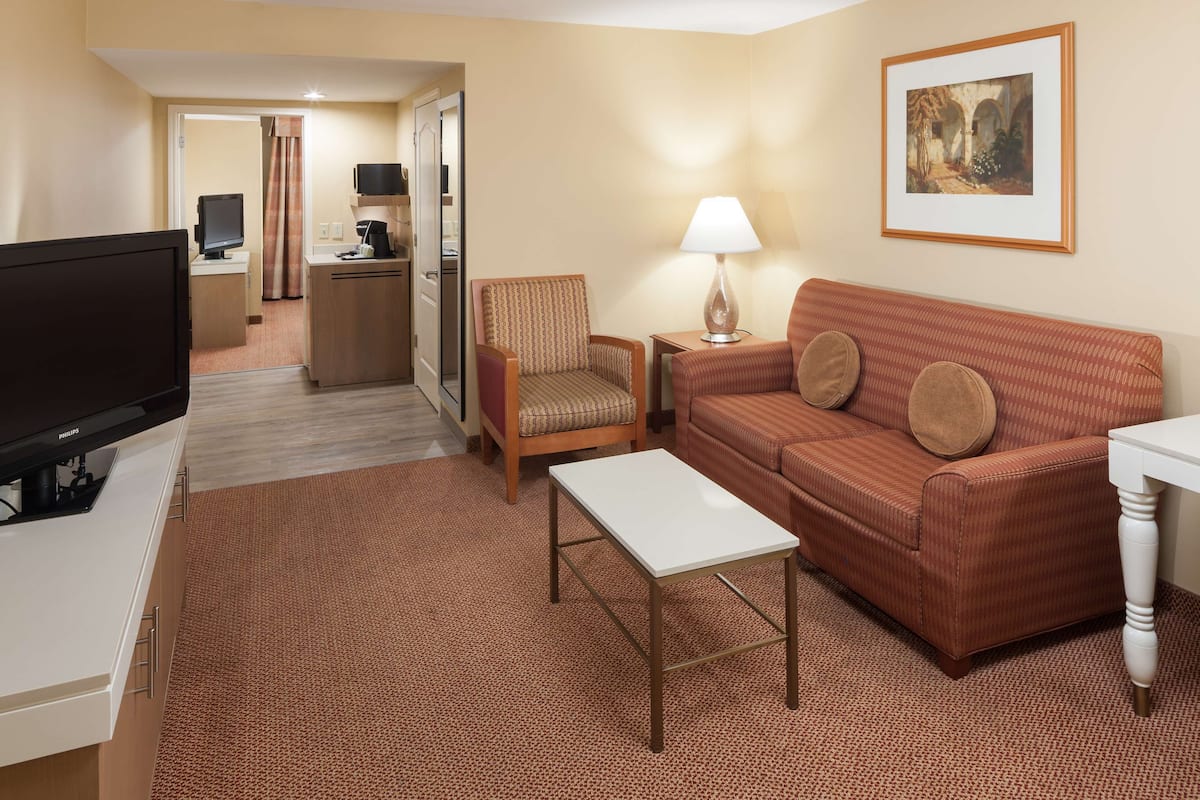 A hotel room with a television, a sofa, a chair, a small table, and a lamp.