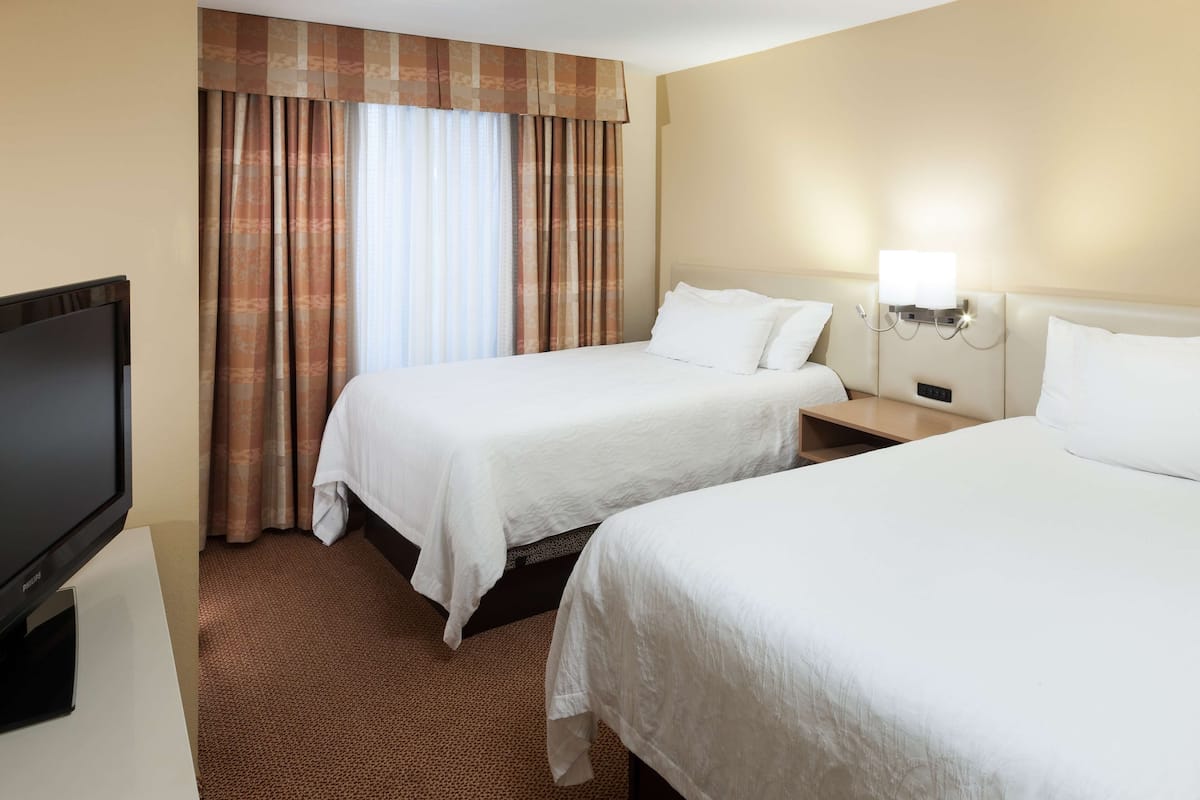 A hotel room with two beds, a TV, and a wall-mounted lamp.