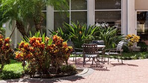 Un espacio de patio al aire libre con piso de ladrillo, rodeado de exuberante follaje y plantas florecientes.