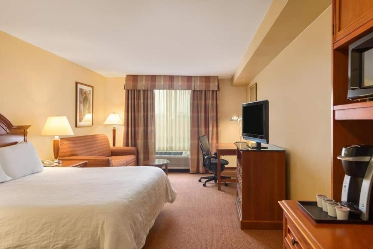A hotel room with a bed, desk, chair, television, and coffee maker.