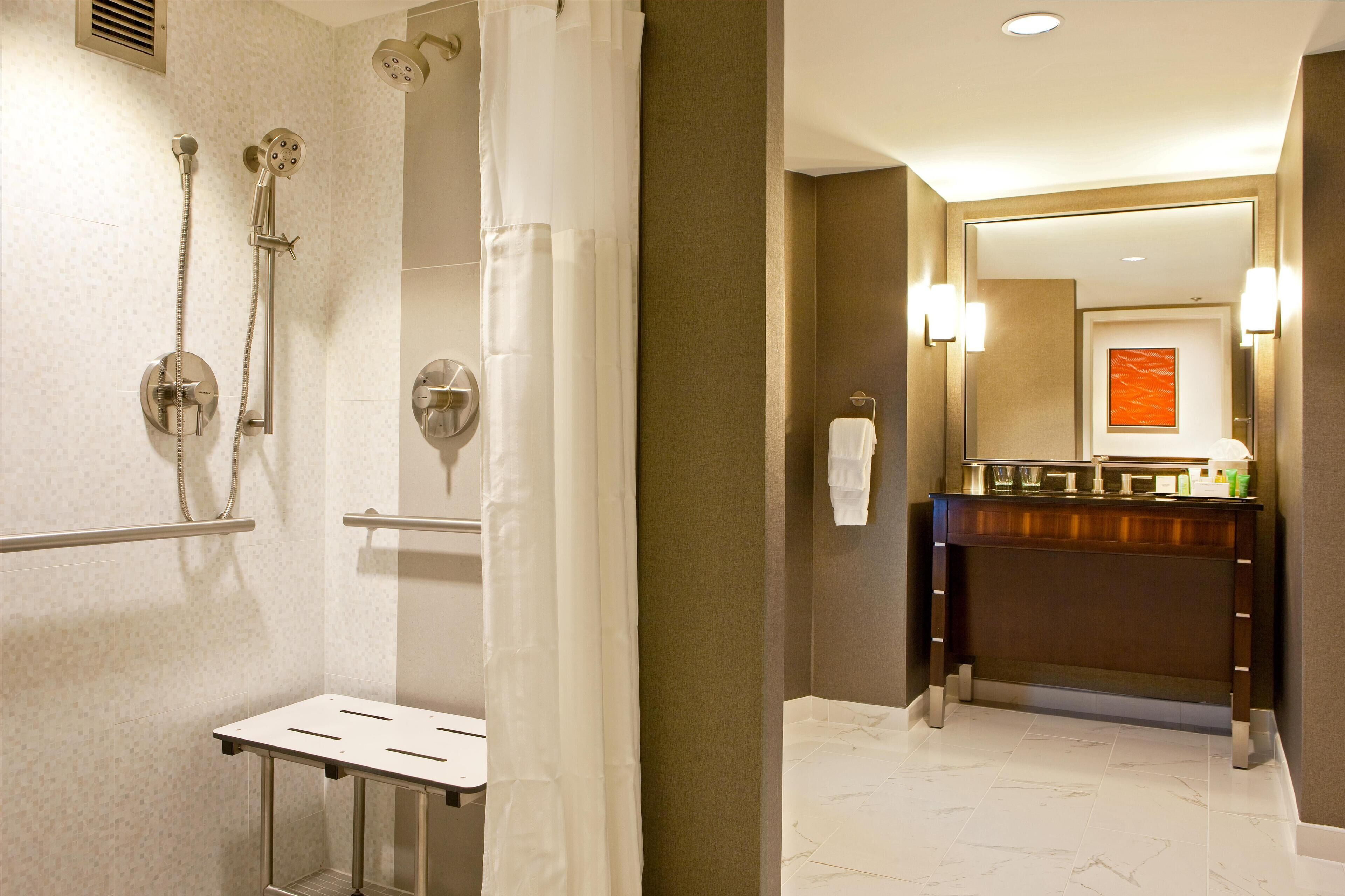 A hotel bathroom with a shower, a sink, a mirror, and a towel rack.