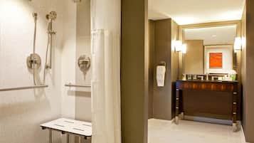 A hotel bathroom with a shower, a sink, a mirror, and a towel rack.